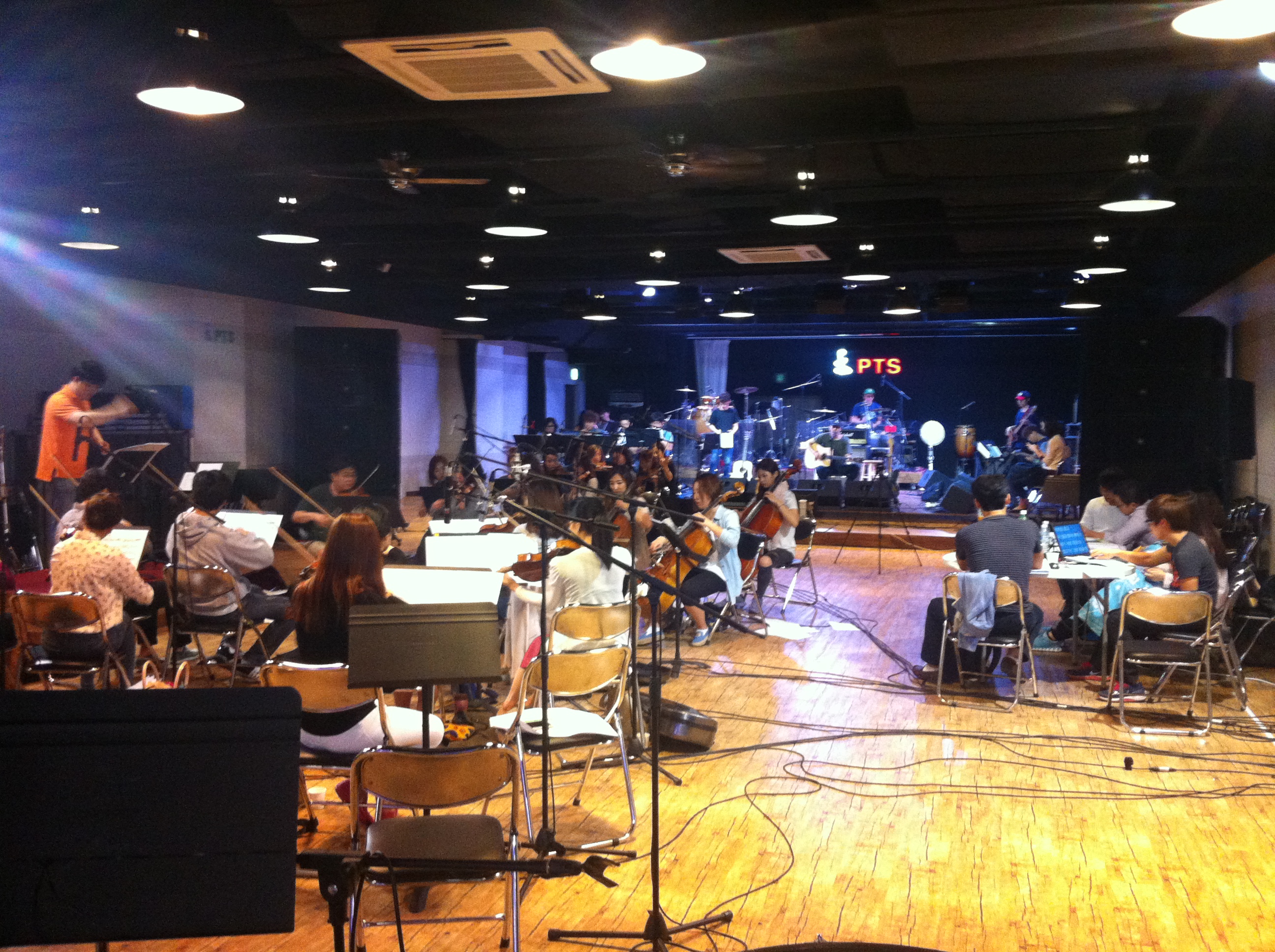 A room filled with musicians playing their instruments, guided by a conductor.