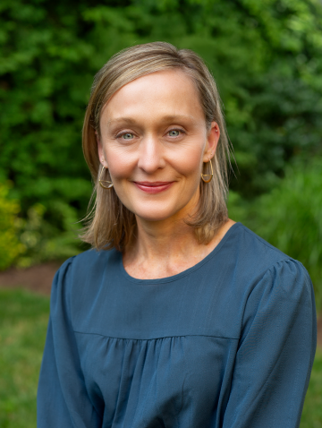 Photo of Kathleen Freis standing in front of some greenery.