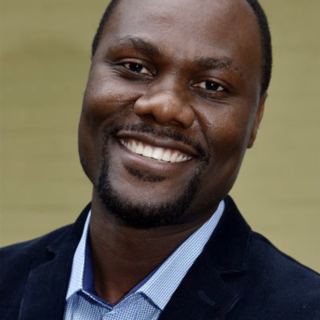 Benedito Machava smiling in a black suit and blue shirt