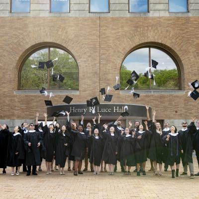 Group of graduates in front of the MacMillan Center throwing caps in the air