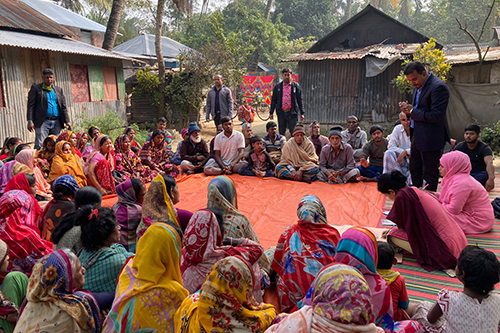 A group of approximately 40 men and women gather outdoors for a meeting in Bangladesh.